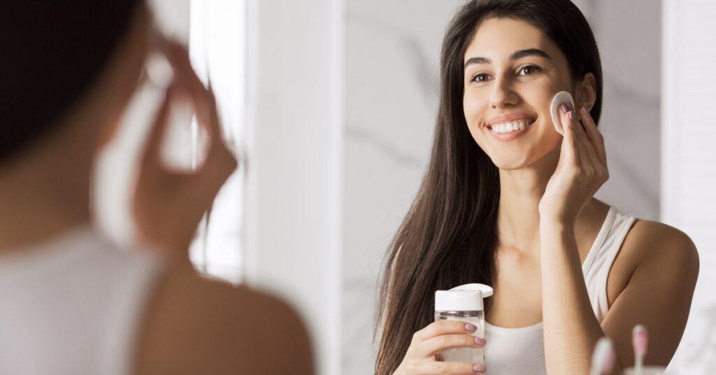 woman using facial cleanser while looking in mirror