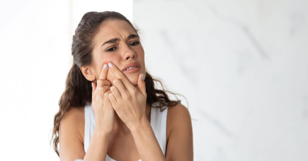 women picking at acne in the mirror