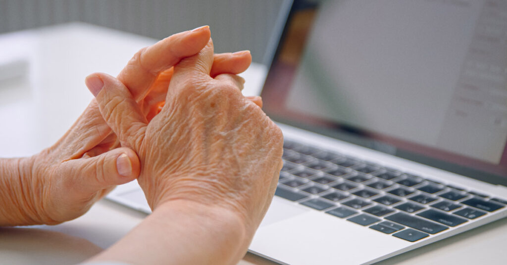 a female manager holds her wrinkled, aging hands over her laptop keyboard